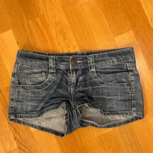 Blå jeansshorts från ONLY - Snygga blå jeansshorts från ONLY med klassisk femficksdesign och slitna detaljer. Shortsen har låg midja, synliga sömmar och bälteshällor. Perfekta för varma dagar när du vill ha en avslappnad och cool stil.