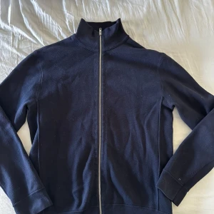 Mörkblå ziptröja från NN07 - Snygg mörkblå ziptröja från NN07 med hög krage och hel dragkedja framtill. Tröjan är i ett mjukt bomullsmaterial och har en clean, minimalistisk look som passar till det mesta. Perfekt för dig som gillar stilrena plagg med enkel design.