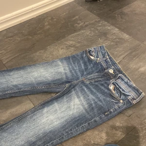 Blå bootcut jeans med slitningar - Snygga blå jeans med bootcut passform och slitna detaljer. Jeansen har klassisk femficksdesign, dragkedja och knapp framtill samt tydliga slitningar och ljusare partier för en cool, använd look. Perfekta för dig som gillar en avslappnad stil.
