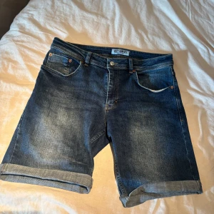 Blå jeansshorts från Just Junkies - Snygga blå jeansshorts från Just Junkies i modellen Mike Shorts. Klassisk femficksdesign, upprullade benslut och cool tvättad denimlook. Perfekta för sommaren och lätta att matcha med allt. Sköna och stilrena shorts för en avslappnad vibe.