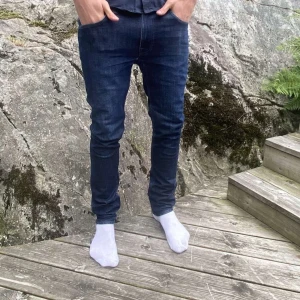 Nudie Jeans - Säljer ett par mörkblå jeans från Nudie Jeans i klassisk femficksmodell. Jeansen har snygga detaljer på bakfickorna och en läderpatch i midjan. Tillverkade i stretchig bomull för en tight och bekväm passform.