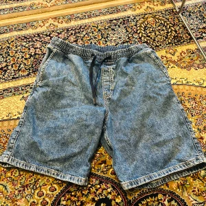 Blå jeansshorts med snörning från H&M - Säljer ett par blå jeansshorts från H&M i regular fit med elastisk midja och svart snörning. Klassisk denimlook med raka ben och sidfickor, perfekta för sommardagar. Sköna och enkla att matcha med allt.