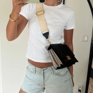 Svart axelväska från Rebecca Minkoff - Snygg svart axelväska från Rebecca Minkoff i skinn med guldfärgat lås och detaljer. Väskan har en bred beige axelrem i textil och flera fack på insidan. Perfekt storlek för det viktigaste och är både stilren och tidlös. Väskan har använts sparsamt och är i fint skick🫶