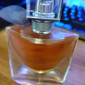 La Vie Est Belle parfym från Lancôme - Elegant parfymflaska från Lancôme, La Vie Est Belle, med en fyrkantig form och rundade kanter. Flaskan är i klart glas med en varm bärnstensfärgad vätska och dekorerad med ett grått tygband runt halsen. Perfekt för dig som gillar lyxiga dofter. Du kan få den billigare ifall du hämtar up den i Solna🙏