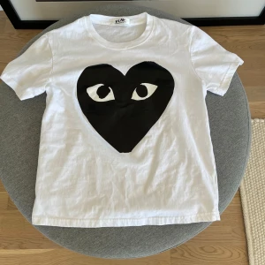 Vit Comme des Garçons Play t-shirt - Vit t-shirt från Comme des Garçons Play med det ikoniska svarta hjärtat med ögon tryckt på bröstet. Klassisk rund hals och korta ärmar. Perfekt för dig som gillar streetstyle och vill sticka ut med en cool detalj. Storlek S men sitter kortare så hade passat någon som är 173 -172 o neråt. Använd endast en gång.