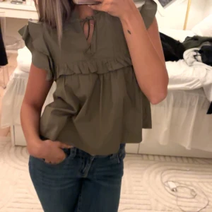 Olivgrön blus med volang och knyt - Supersöt olivgrön blus med volangdetaljer från Gina tricot!