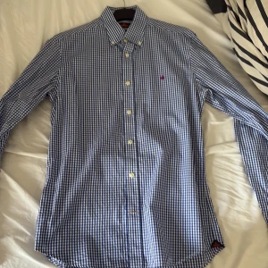 Blårutig skjorta från Morris, S - Snygg blårutig skjorta från Morris med klassisk krage och knappar framtill. Skjortan har lång ärm och är tillverkad i bomull. Broderad lila logga på bröstet ger en extra detalj. Perfekt för dig som gillar stilrena och tidlösa plagg.