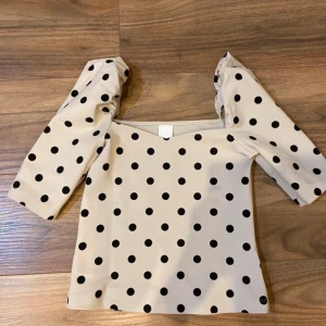Prickig topp med puffärm från H&M - Beige topp från H&M med svarta prickar och puffärmar. Köpt på vinted men aldrig använt och den är i bra skick, lånade bilder💗