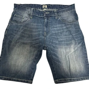 Blå jeansshorts från Denim, stl 30 - Klassiska blå jeansshorts från Denim med fem fickor, normal passform och snygga slitningar. Shortsen har bälteshällor, dragkedja och knapp framtill. Perfekta för varma dagar och en avslappnad stil.