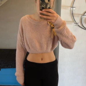 Croppad stickad tröja med snörning i ryggen  - Superfin croppad stickad tröja i ljusrosa med långa ärmar och cool snörning i ryggen. Tröjan har hål i vardera ärm, dock sitter de på insidan av tröjan vilket gör att man inte tänker på det! Går att ha tummarna i om man föredrar det😉Snygg till både jeans och kjol.