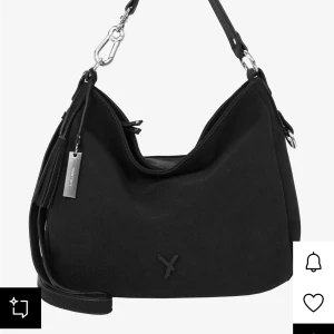 Svart axelväska från Suri Frey - Snygg svart axelväska från Suri Frey med stilren design och silvriga metalldetaljer. Väskan har en mjuk, lätt strukturerad yta i syntetmaterial, dragkedja upptill och flera innerfack. Perfekt för dig som vill ha plats för allt du behöver i vardagen.  Höjd- 20cm, längd- 33cm, bredd- 15cm och handtaget är 30cm. Köpt för 680kr