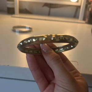 Guldigt armband med nitar - Coolt armband i guldig metall med markerade pyramidformade nitar runt hela. Ger en edgy vibe och passar perfekt för att lyfta din outfit. Rund och stel modell som är enkel att matcha med andra smycken.