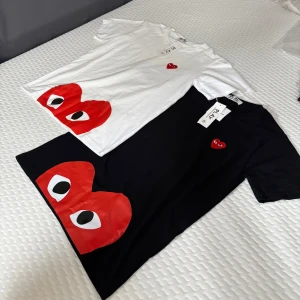 Svart t-shirt Comme des Garçons Play - Svart t-shirt från Comme des Garçons Play med ikoniskt rött hjärta med ögon tryckt nertill och broderat på bröstet. Klassisk rund hals och kort ärm. Tillverkad i mjuk bomull, perfekt för en clean och cool look.