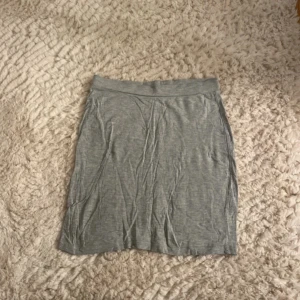 Grå basic kjol från Bik Bok - Enkel och mjuk grå kjol från Bik Bok i stretchig bomull. Modellen är rak och kort, perfekt till sneakers eller sandaler. Resår i midjan för skön passform. Snygg att matcha med en crop top eller hoodie.