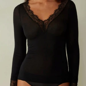 Intimissimi  - Snygg svart långärmad blus med djup v-ringning och spetsdetaljer längs halsringningen och ärmsluten. Toppens material är tunt och följsamt, vilket ger en elegant och feminin look. Perfekt för dig som gillar stilrena och trendiga plagg.