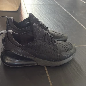 Svarta Nike Air Max 270 sneakers - Säljer ett par helsvarta Nike Air Max 270 sneakers med stor synlig luftbubbla i hälen och ventilerande mesh-ovandel. Skorna har snörning och en sportig vibe, perfekt för dig som gillar streetstyle. Snygg och modern design med diskreta loggor på sidan. Passar dig som bär storlek 38/39 