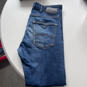 Emporio Armani jeans - Snygga blå jeans från Emporio Armani med klassisk femficksdesign och logga på bakfickan. Jeansen har en rak passform och är tillverkade i mjukt denimtyg med snygga slitningar och kontrastsömmar. Perfekta för en stilren och avslappnad look.