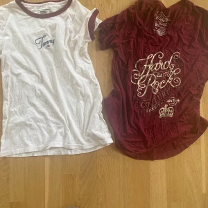 2 t-shirts: Tommy Hilfiger & Hard Rock - Två snygga t-shirts! En vit Tommy Hilfiger med vinröda detaljer och broderad logga, samt en vinröd Hard Rock Couture med guldig text och v-ringning. Båda är kortärmade och perfekta för dig som gillar klassiska och coola tryck. XS storlek.
