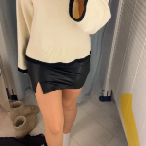 Svart skinnkjol med slits - Snygg svart kort skinnkjol med en liten slits framtill. Kjolen har en tight passform och ger en cool vibe till outfiten. Perfekt för dig som gillar trendiga och stilrena plagg.