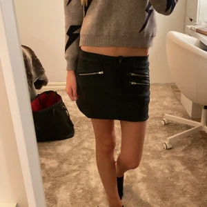 Svart kortkjol med dragkedjor - Snygg svart kortkjol med flera coola dragkedjor framtill. Kjolen har en rak passform och midjehög modell som ger en trendig look. Perfekt att matcha med en stickad tröja eller crop top för en chill vibe.