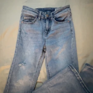 Ljusblå bootcut jeans med slitning - Snygga ljusblå jeans med bootcut-ben och en liten slitning på ena låret. Klassisk femficksmodell i mjukt denimtyg, perfekt för dig som gillar en avslappnad och trendig look. Passar till sneakers eller boots.