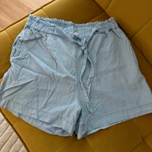 Ljusblå shorts med knyt från H&M - Superbekväma ljusblå shorts från H&M med elastisk midja och knytband framtill. De har två sidfickor och två bakfickor för en chill look. Perfekta för varma dagar och lätta att matcha med allt. Materialet känns mjukt och luftigt.