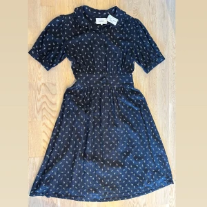 Svart blommig klänning från ba&sh - Supersöt svart klänning från ba&sh med små vita blommor, markerad midja och kort ärm. Klänningen har knappar framtill, krage och lätt utställd kjol som slutar strax ovanför knäna. Perfekt för dig som gillar en feminin och tidlös stil, klänningen har underklänning. Nyligen köpt på secondhand för 595:- säljes då den är lite liten för mig. Två mindre defekter som man ej tänker på – se sista bilden! 100% bomull.