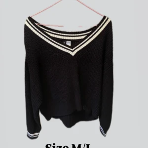 Svart stickad v-ringad tröja M/L - Svart stickad tröja med v-ringning och vita ränder längs halsringningen och ärmsluten. Tröjan har en loose passform och långa ärmar, perfekt för lager-på-lager och chill stil.