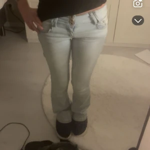 Ljusblå bootcut jeans  - Snygga ljusblå jeans från med bootcut passform och låg midja. Jeansen har tre guldiga knappar framtill, klassiska fickor och bälteshällor. Perfekta för dig som gillar en retro vibe och vill ha ett par jeans som sticker ut lite extra. Inga slitningar, precis som nya.