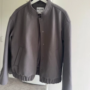 Grå bomberjacka från NA-KD - Säljer en stilren grå bomberjacka från NA-KD med rund krage och tryckknappar framtill.  Oversized passform🌸