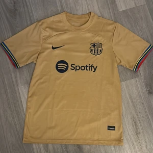 FC Barcelona guld fotbollströja   - FC Barcelona matchtröja helt ny oanvänd, perfekt till dig som vill toppa stilen en varm sommardag eller använda till fotbollsträningen. Storleken är medium men den är lite större än det så jag skulle säga att det blir M/L