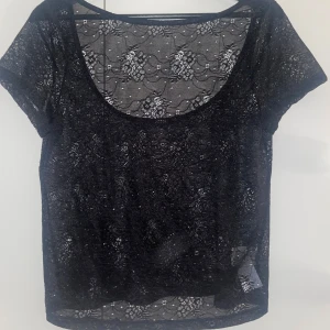 Svart spetsblus med kort ärm - Jag säljer en svart blus i transparent spets ifrån Bikbok i storlek M (men passar även som S). Modellen är öppen i ryggen och korta ärmar med blommigt mönster. Jag har aldrig använt den. Pris kan diskuteras. Perfekt till sommaren🥰