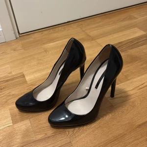 Svarta lackpumps med hög klack - Snygga svarta pumps i glansigt lackmaterial från Zara Woman. Skorna har spetsig tå och hög smal klack som ger en elegant siluett. Perfekta för dig som vill sticka ut med en klassisk och stilren look.