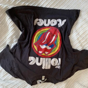 Rolling Stones t-shirt från H&M - Svart t-shirt från H&M med Rolling Stones ikoniska tunga-logga i regnbågsfärger och vit text. Klassisk passform och rund hals. Det står storlek M men sitter nog som en S. Köpt för ganska högt pris och fint använd därav priset