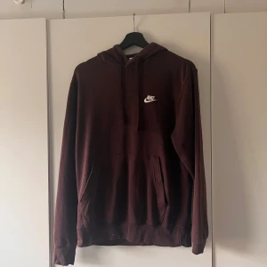 Mörkbrun Nike hoodie med huva - Säljer en mörkbrun hoodie från Nike med vit broderad logga på bröstet. Tröjan har huva med snörning och en stor känguruficka framtill. Perfekt för chill dagar och streetstyle. Långärmad och i mjukt bomullsmaterial.