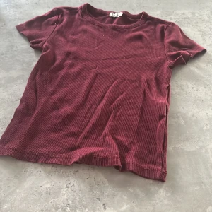 Vinröd ribbad t-shirt   - Vinröd t-shirt från Cubus  i storlek 146/152. T-shirten är ribbad och har korta ärmar samt rund halsringning. Materialet känns mjukt och stretchigt, perfekt för en chill och stilren look.