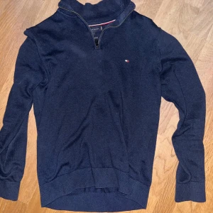 Marinblå half zip - Snygg marinblå tröja från Tommy Hilfiger med half zip och liten logga på bröstet. Tröjan är gjord i premium bomull och har ribbade muddar vid ärmslut och nederkant. Perfekt för dig som gillar stilrena och klassiska plagg med en modern touch.