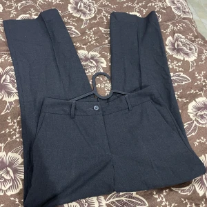 Mörkgrå kostymbyxor från H&M - Snygga mörkgrå kostymbyxor från H&M i klassisk rak modell med bälteshällor och knappstängning.  OBS Dom ser större ut på bild! Kontakta för bilder på! Storlek 36
