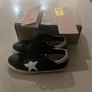 Golden goose skor  - Golden Goose sneakers i svart skinn med vit stjärndetalj på sidan och vit kant runt hälen. Klassisk låg modell med rund tå och platt sula.  Snygga och stilrena för dig som gillar streetstyle.