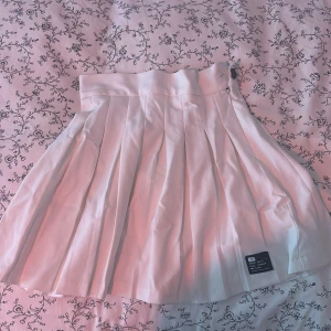 Vit plisserad kjol från Bershka XS - Supersnygg vit plisserad kjol från Bershka i storlek XS. Kjolen har bred linning och klassiska veck som ger en preppy vibe. Perfekt för dig som gillar stilrena och trendiga plagg. Materialet känns lätt och bekvämt, och kjolen stängs med dragkedja i sidan.