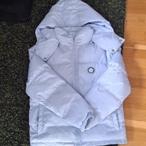 Ljusblå pufferjacka från Trapstar XS - Säljer en ljusblå pufferjacka från Trapstar i storlek XS. Jackan har huva, dragkedja framtill, två fickor med tryckknapp och Trapstar-logga på bröstet samt stor broderad text på ryggen. Perfekt för kalla dagar och riktigt snygg streetstil.