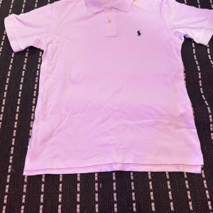 Vit pikétröja från Ralph Lauren - Klassisk vit pikétröja från Polo Ralph Lauren med korta ärmar och broderad marinblå logga på bröstet. Tröjan har krage och två knappar framtill. Tillverkad i mjuk bomull för en bekväm känsla och snygg passform.