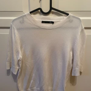 Vit stickad tröja från lager 157 - En stilren vit stickad tröja från lager 157 med rund halsringning och korta ärmar. Tröjan har en enkel och clean look som passar perfekt till jeans eller kjol. Ribbad kant vid halsen och ärmsluten ger en snygg detalj.