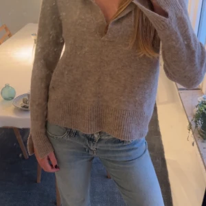 Beige stickad tröja Twist & Tango - Supermjuk beige stickad tröja från Twist & Tango med krage och v-ringning. Tröjan har långa ärmar och breda ribbade muddar vid ärmslut och nederkant. Perfekt för lager-på-lager och chill vibes.