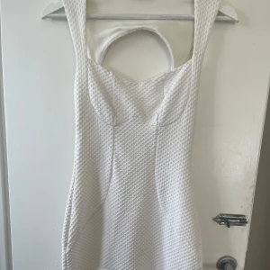Vit strukturerad kortklänning - Supersnygg vit vintage klänning med strukturerat tyg och markerad byst. Klänningen har breda axelband, rund uringning och en cool cut-out detalj i ryggen. Passformen är figurnära och nederdelen har en lätt volang. Perfekt till studenten, fester, middagar mm. Passar XS-S