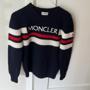 Randig stickad tröja från Moncler - Snygg stickad tröja från Moncler i marinblått med vita och röd loga och en liten moncler loga på armen. köpt på farfetch för 4000. Priset är diskuterbart. Säljer den för att jag har växt ur den och nu vill ja tjärna lite pengar.