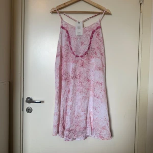 Rosanna Garden Pink klänning M - Superfin ljusrosa och vit kortklänning från Rosanna med tunna axelband och ett unikt mönste från märket Fira. Klänningen har glittriga detaljer och en lös passform, perfekt för sommarens varma dagar. Snyggt fall och v-ringad framtill med dekorativ kant. Storlek M. Helt ny med tags/ prislapp fortfarande kvar. 