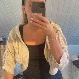 Beige stickad bolero - Säljer en beige stickad kofta med kort, croppad passform och ballongärmar. Koftan har bred ribbad mudd och ett öppet, avslappnat snitt.
