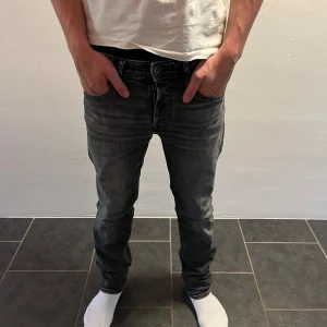 Grå slim fit jeans från Jack & Jones - Snygga grå jeans från Jack & Jones (L32 och W29). Jeansen har en slim fit passform och är tillverkade i mjukt denim-material som sitter skönt hela dagen. Perfekt för dig som gillar en modern och stilren look.