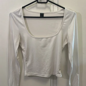 Vit långärmad topp från SHEIN XS - En stilren vit långärmad topp från SHEIN i storlek XS. Toppen har en djup, fyrkantig urringning och är figurnära i modellen. Tillverkad i ett mjukt och stretchigt material som känns skönt mot huden. Perfekt att matcha med jeans eller kjol för en clean look.